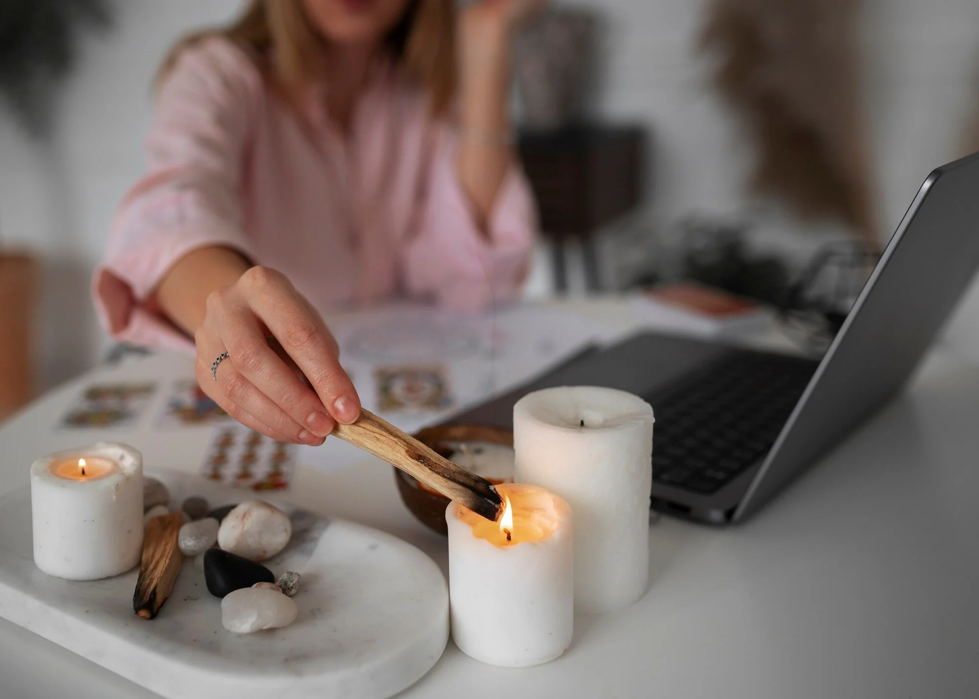 Mum alevinde Palo Santo çubuğunu yakan kadın, masada taşlar ve dizüstü bilgisayar