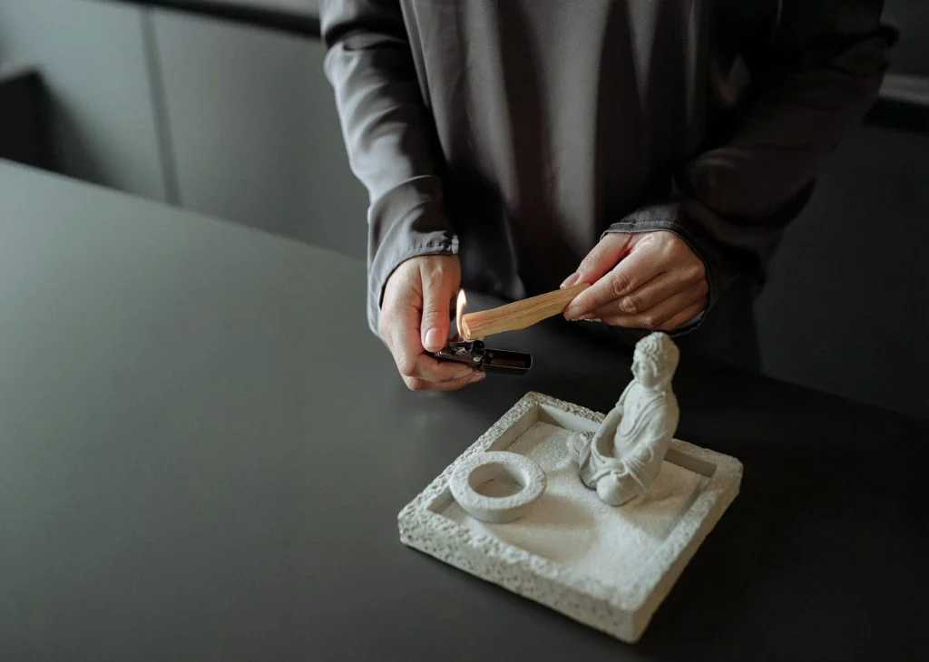 Ağaç Tütsüler Nasıl Kullanılır? Palo Santo, Sandal ve Öd Ağacı Rehberi Beyaz taş tütsülük üzerinde Palo Santo çubuğunu çakmakla yakan eller
