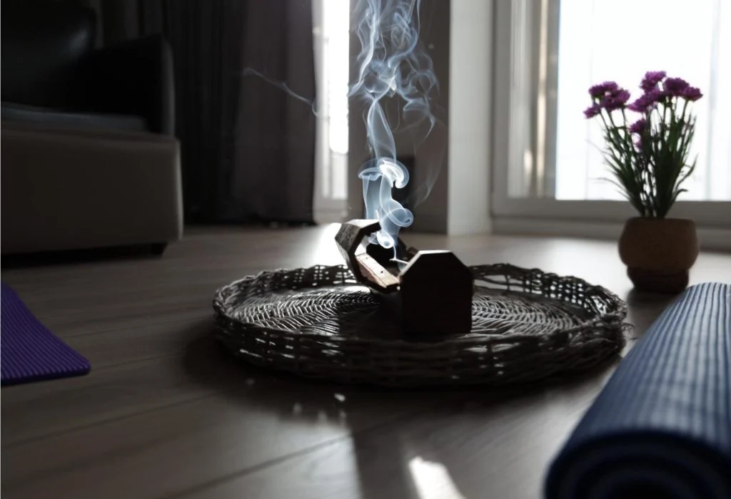 Ud Kokusu Nedir? Ud Tütsüsüyle Meditasyon Rehberi Oturma odasında hasır tepside dumanı tüten tütsülük, yanında yoga matı ve saksıda çiçek